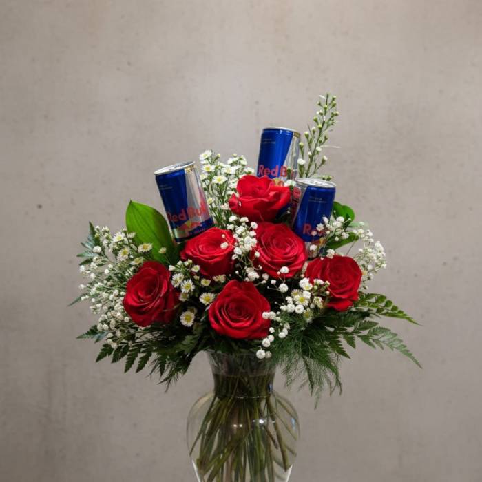 Red roses in a glass vase with Red Bull cans and small white filler flowers