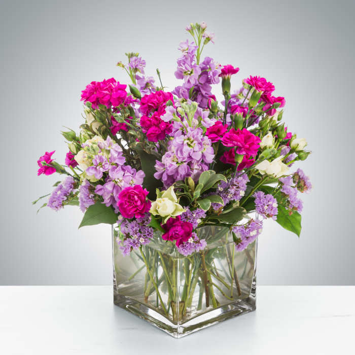 Low arrangement of pink and lavender flowers with white blooms in a clear glass cube vase