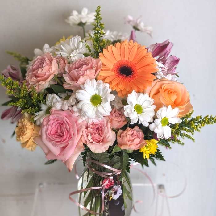 Mixed bouquet of pink roses, white daisies, and an orange gerbera daisy in a clear glass vase