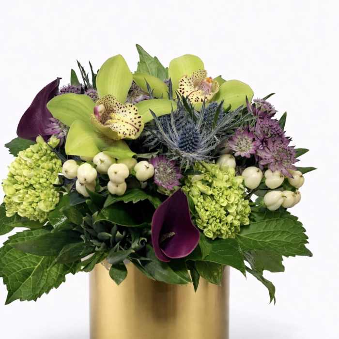 Mixed floral arrangement in a gold cylinder vase with green orchids and purple blooms