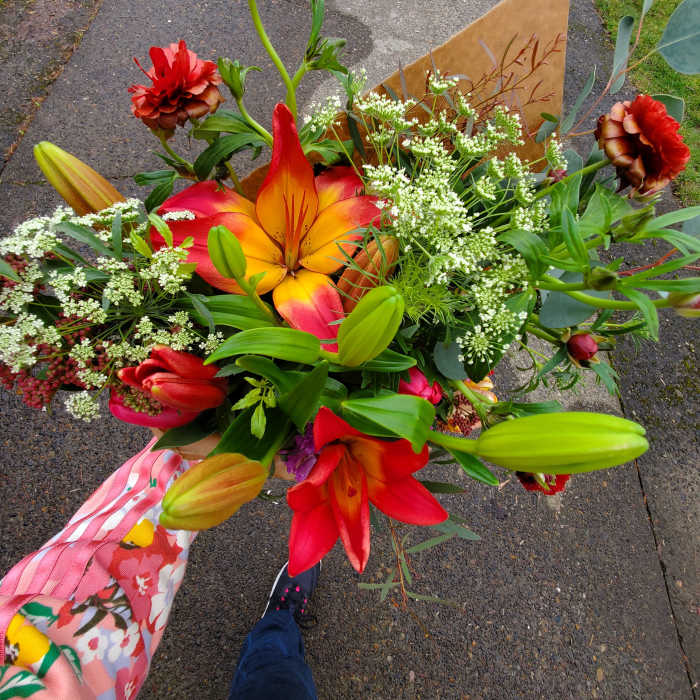 Handheld bouquet of red and orange lilies with small white filler flowers in kraft paper wrap