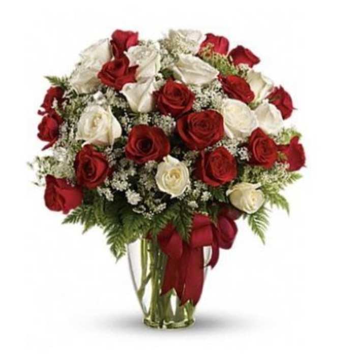 Arrangement of red and white roses with small white filler flowers in a clear glass vase with a red bow.