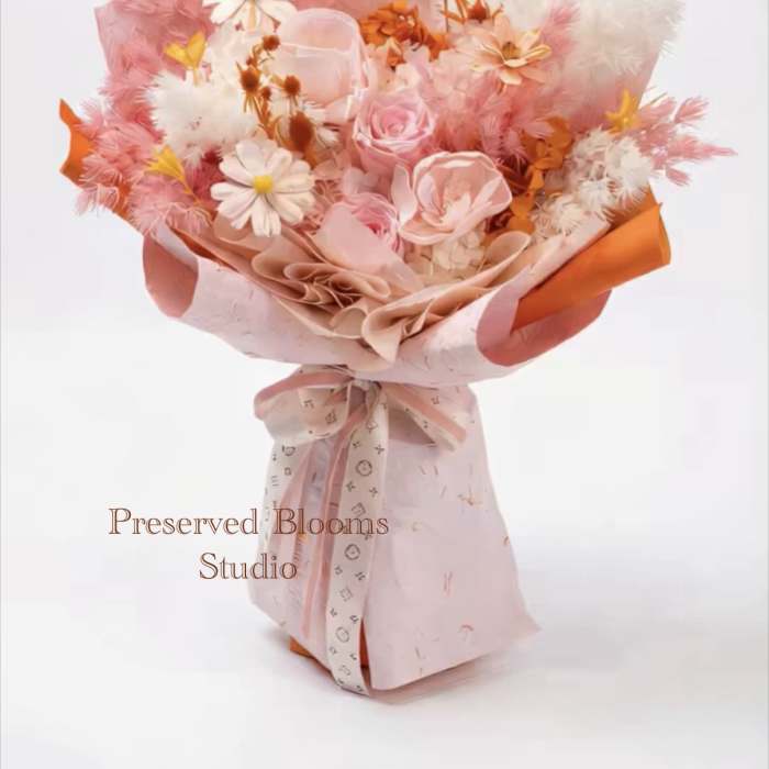 Pink and white bouquet of roses and daisy-like blooms wrapped in pink and orange paper with a bow.