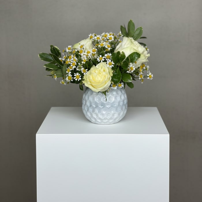 Yellow roses and white daisies in a textured white vase