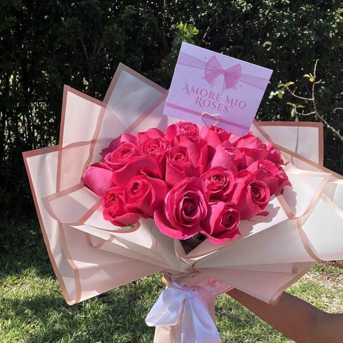 Bouquet of bright pink roses wrapped in blush paper with a white ribbon