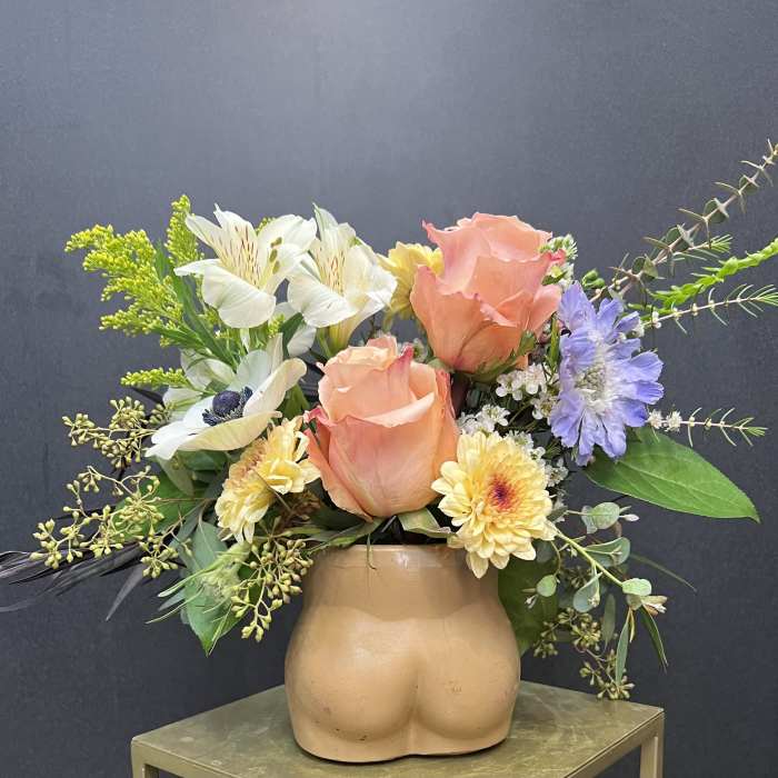 Peach roses and mixed flowers in a tan ceramic vase shaped like a torso