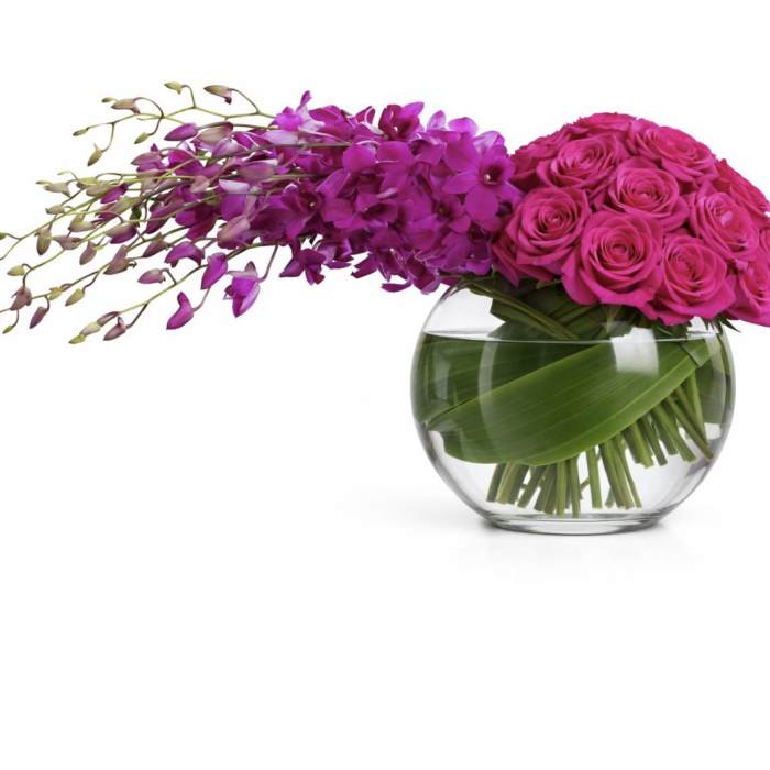 Pink roses and purple orchids in a glass bowl vase