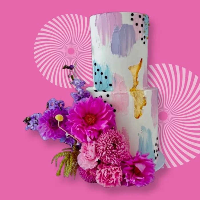 Pink floral arrangement beside a painted two-tier cake