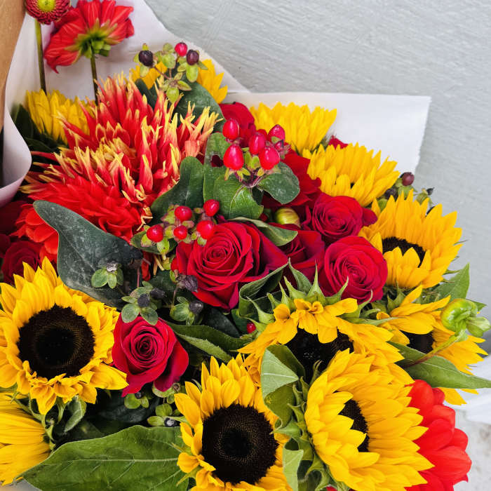 Bouquet of red roses and yellow sunflowers wrapped in white paper