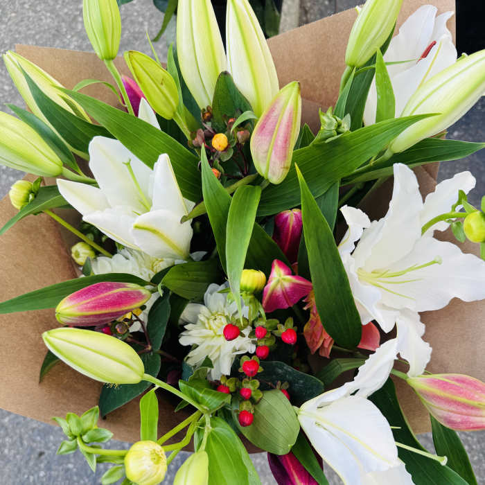Bouquet of white and pink lilies with red berries wrapped in brown kraft paper
