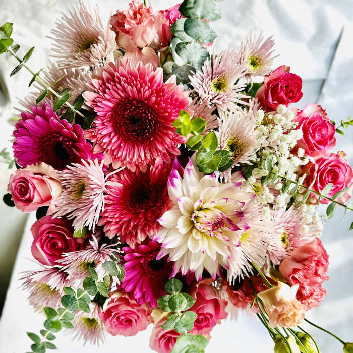 Bright bouquet of pink gerbera daisies, roses, and mixed blooms with trailing eucalyptus.