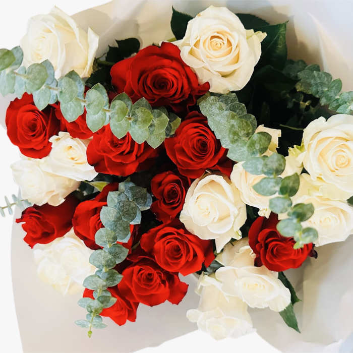 Hand-tied bouquet of red and cream roses with eucalyptus in white paper wrap