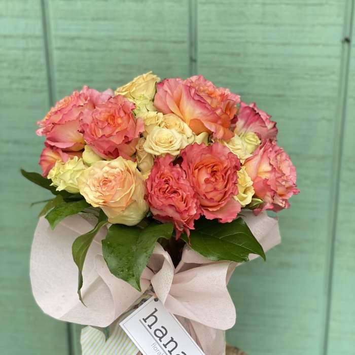 Pink and peach roses in a wrapped bouquet with a ribbon tag