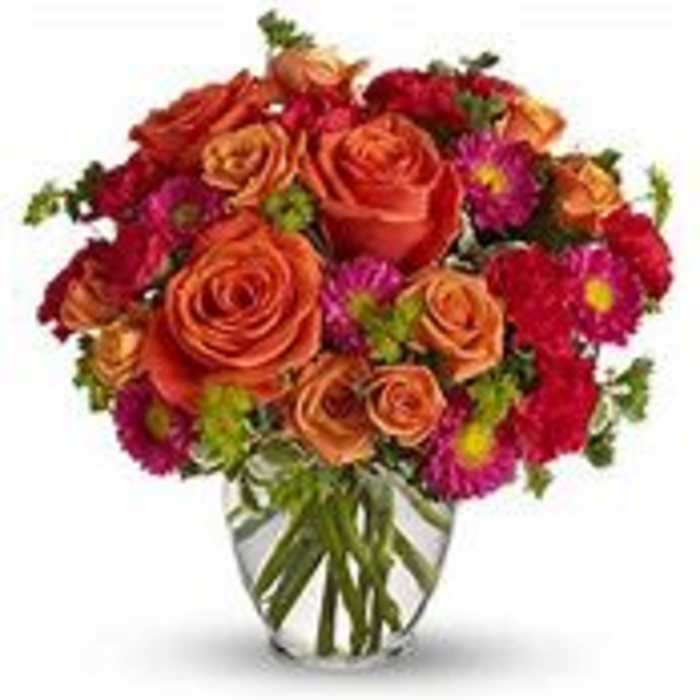 Bouquet of orange roses and magenta daisies in a clear glass vase
