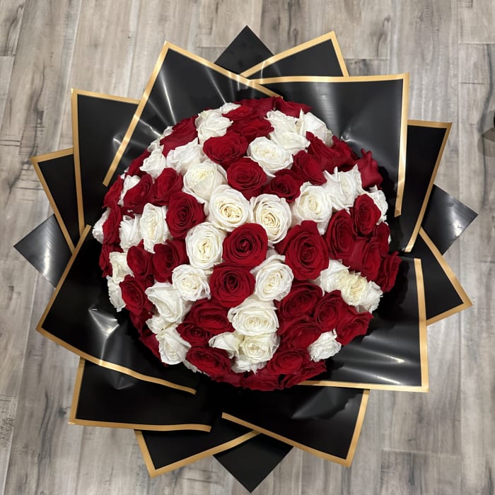 Round bouquet of red and white roses wrapped in black paper with gold trim