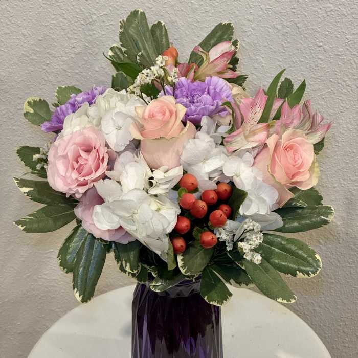 Pink and white mixed bouquet with purple accents and red berries in a faceted dark purple glass vase