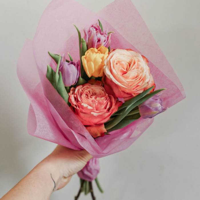 Handheld bouquet of pink and peach tulips wrapped in pink paper