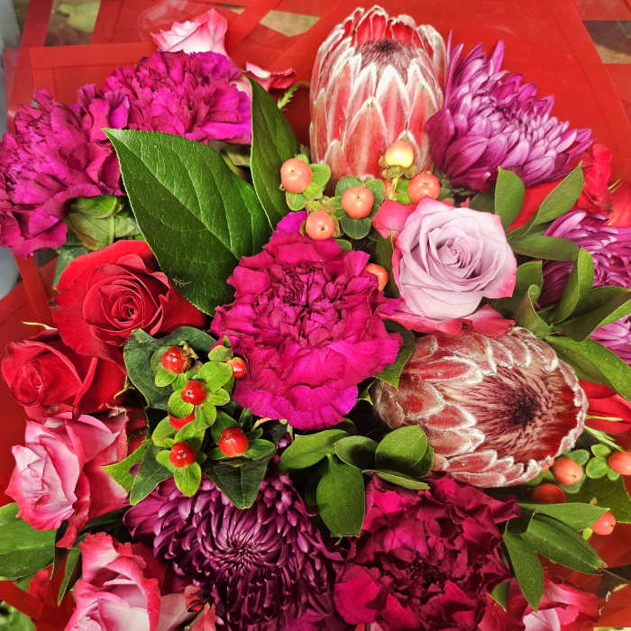 Bouquet of pink and purple flowers with red roses and green foliage