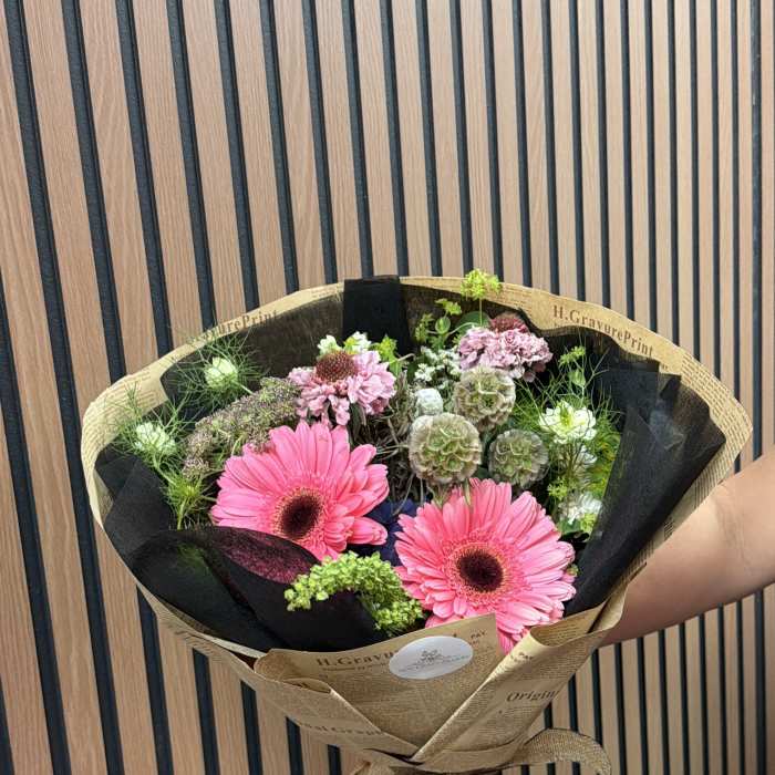 Bouquet of pink gerbera daisies and mixed blooms wrapped in brown paper