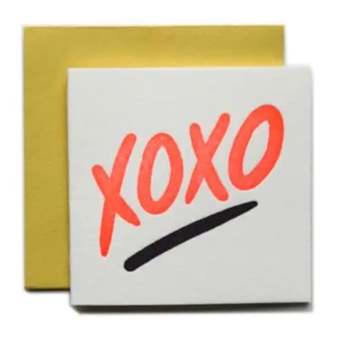 Square white greeting card with neon orange XOXO text and black underline, with a yellow envelope behind it