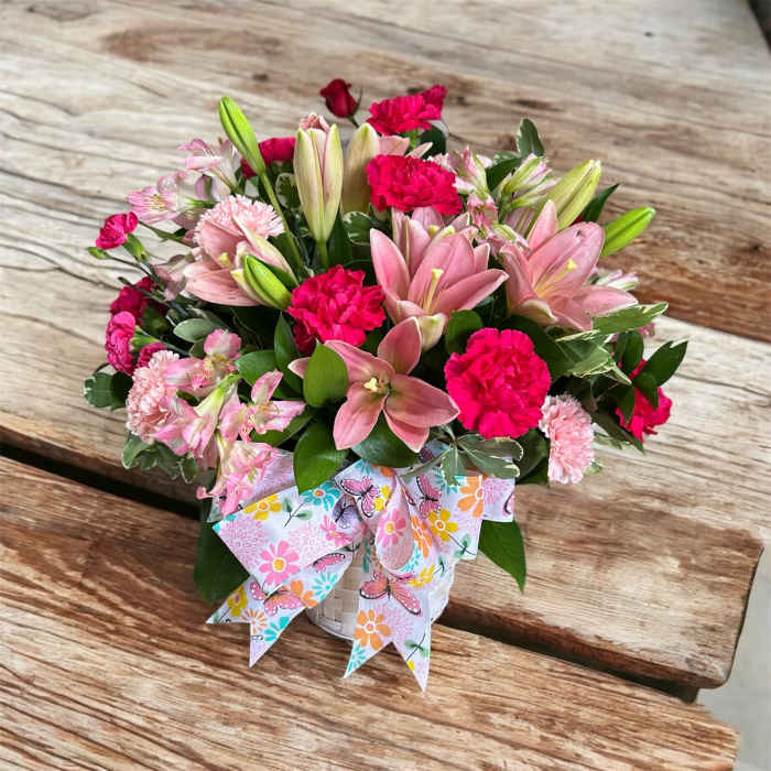Basket arrangement of pink lilies and carnations with a floral butterfly ribbon.