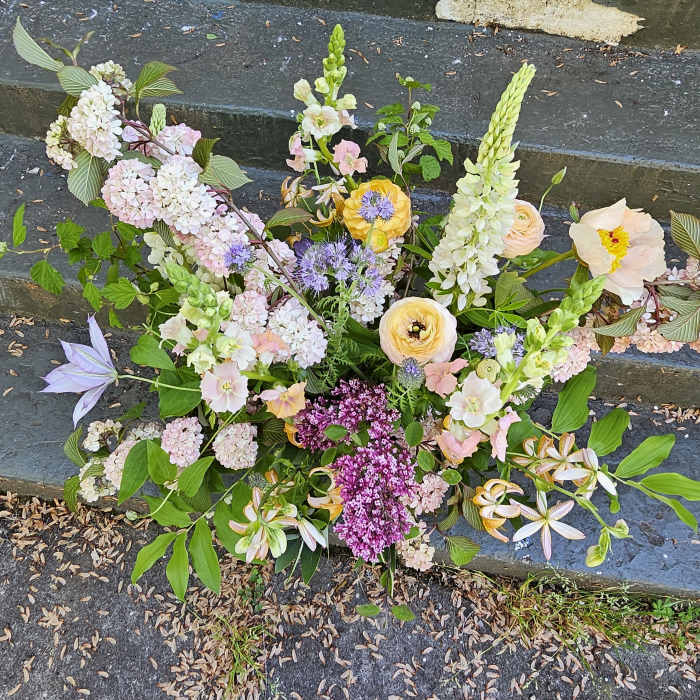 Loose garden-style arrangement of pastel flowers with purple accents displayed on outdoor stone steps