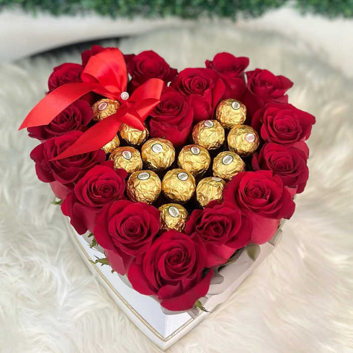 Heart-shaped box of red roses with gold-wrapped chocolates and a red ribbon