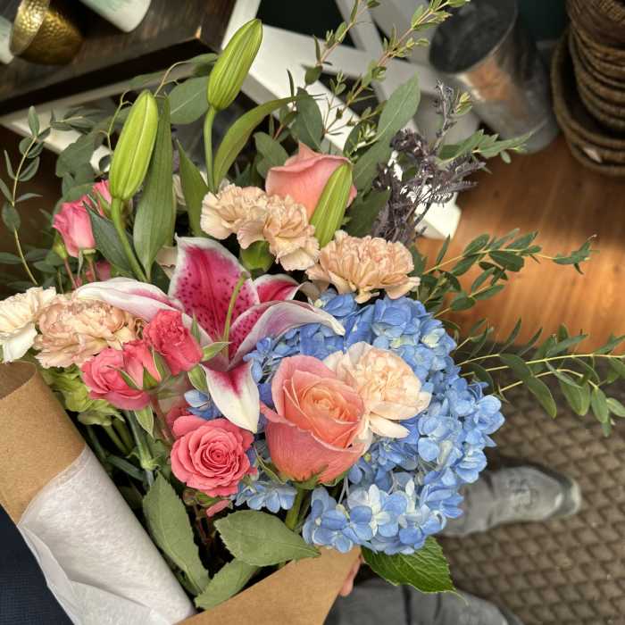 Hand-tied bouquet with pink roses, blue hydrangeas, lilies, and carnations