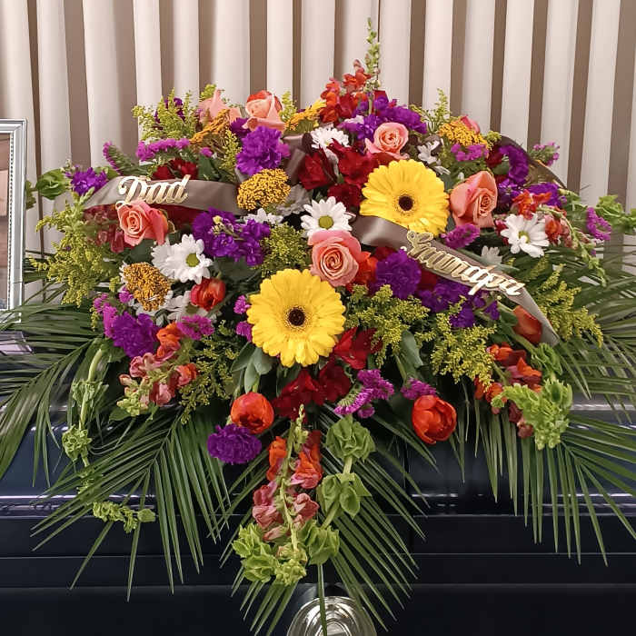 Large funeral spray with mixed flowers and ribbons on a stand