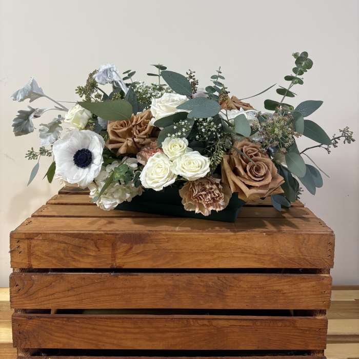 Low floral arrangement with white and tan roses in a dark container