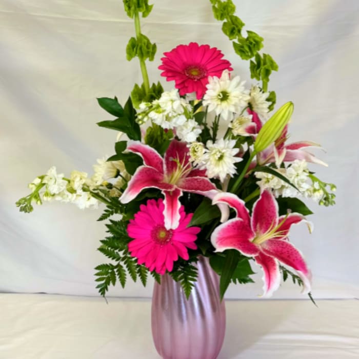 Tall pink and white arrangement with lilies and gerbera daisies in a pink vase with arching green bells of Ireland