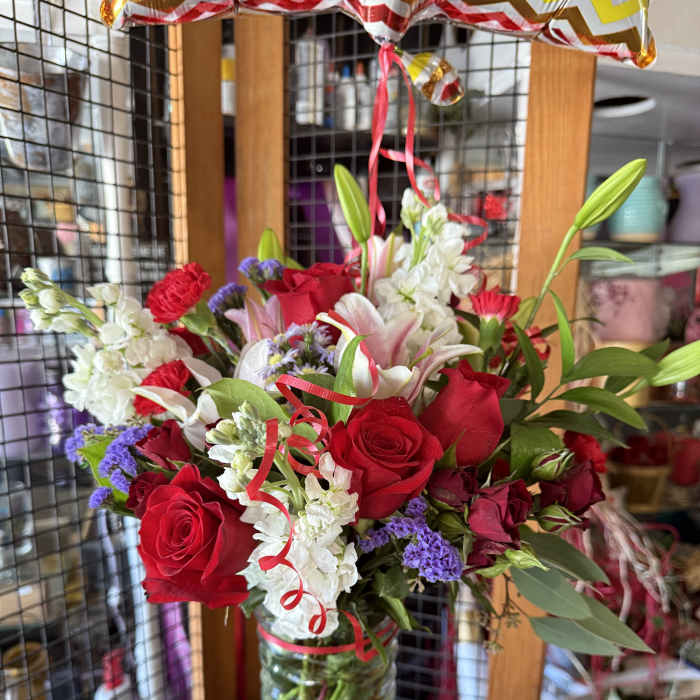 Red roses and lilies arranged in a glass vase with ribbon curls