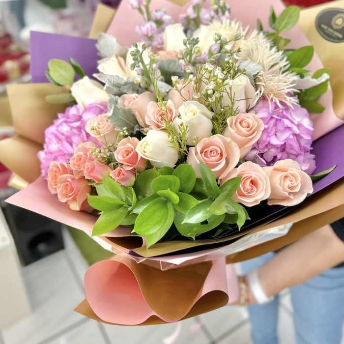 Hand-tied bouquet of pink and cream roses with hydrangeas and mixed blooms in pastel wrapping paper