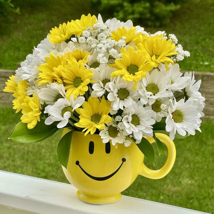 Yellow and white daisy bouquet in a smiley-face mug