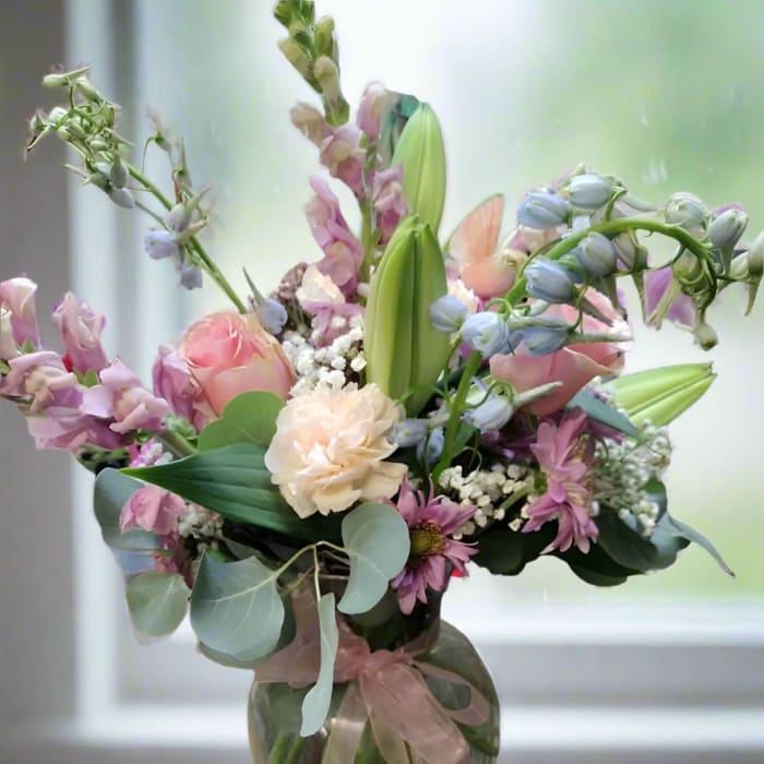 Pastel bouquet of mixed flowers in a glass vase with a ribbon