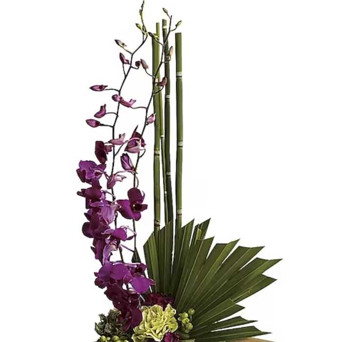 Tall floral arrangement with purple orchids and green fan leaves on a wooden base