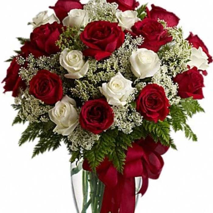 Red and white roses in a clear glass vase with a red ribbon