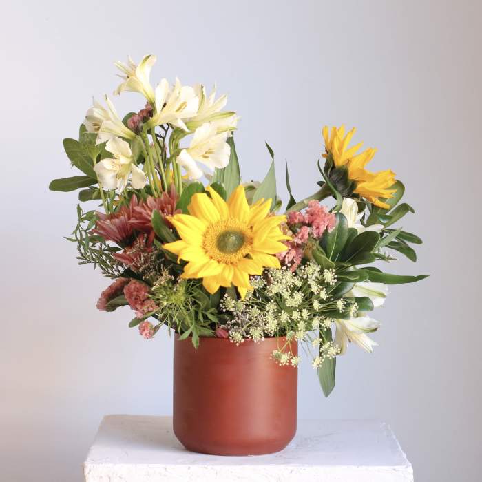 Mixed bouquet with sunflowers, white lilies, and pink flowers in a red vase