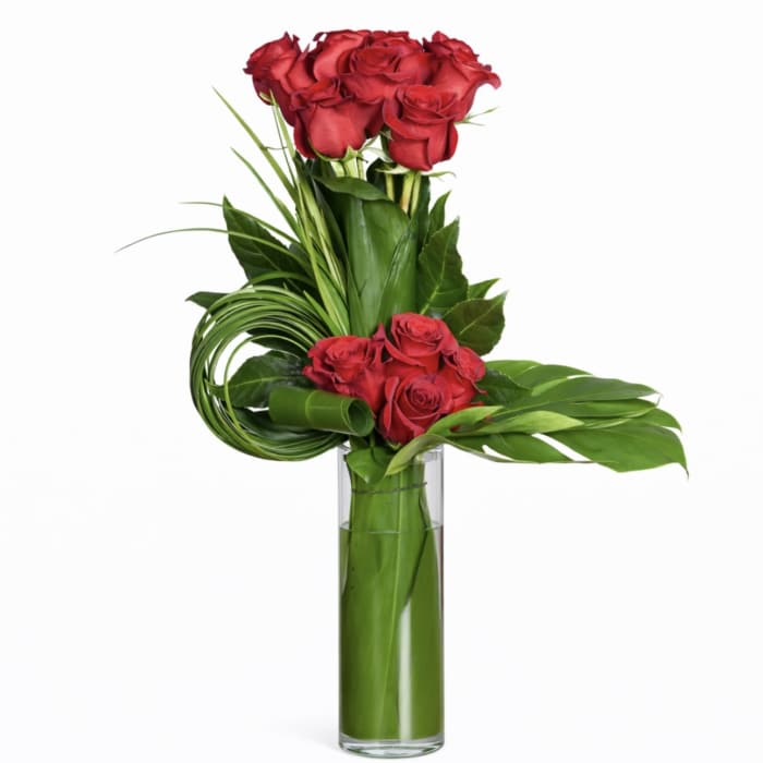 Red roses arranged in a tall glass vase with broad green leaves
