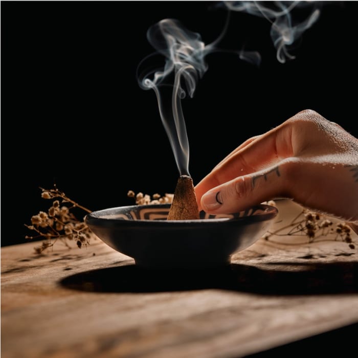 Hand lighting incense in a small bowl on a wooden surface