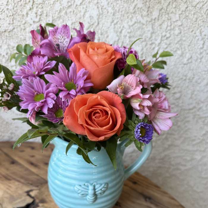 Bouquet of orange roses and purple daisies in a blue ceramic pitcher