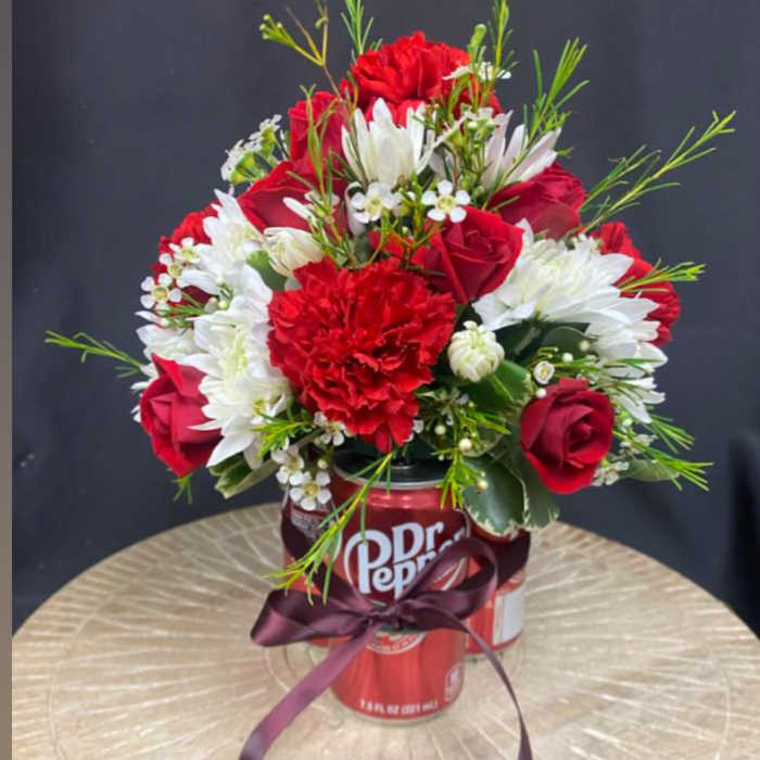 Red and white flower arrangement in a Dr Pepper can with a ribbon