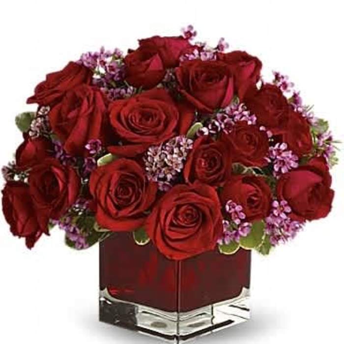 Low square arrangement of red roses with small pink blooms in a red glass cube vase