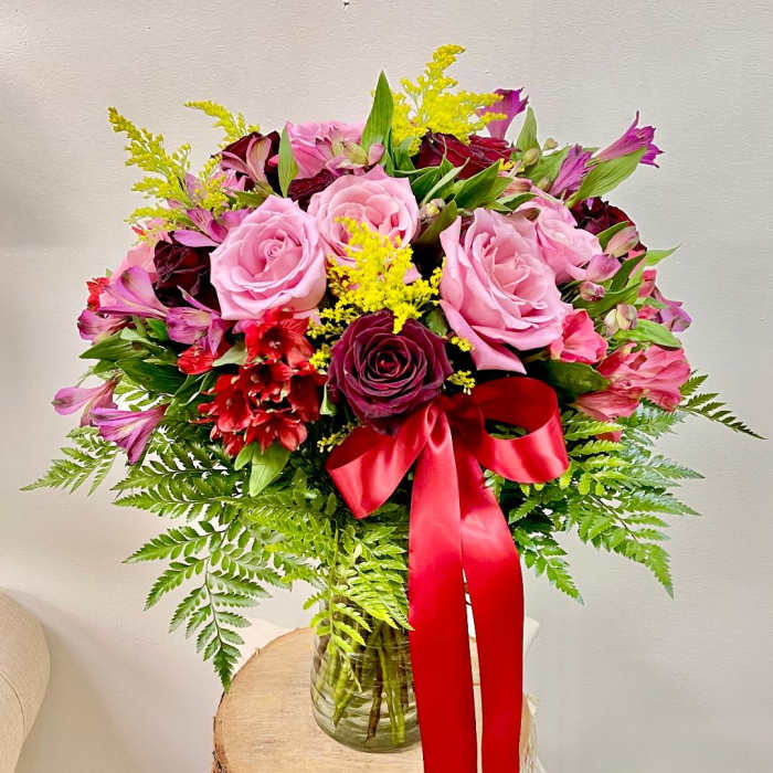 Pink and burgundy rose bouquet in a glass vase with a red ribbon