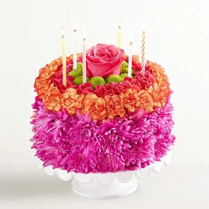 Flower-covered cake with candles and a pink rose on top