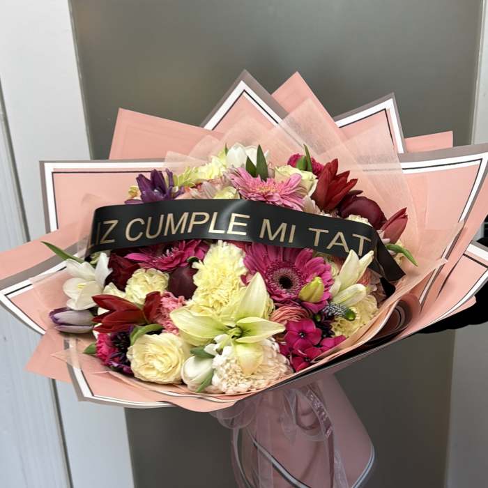 Mixed bouquet of pink, red, white, and yellow flowers wrapped in pink paper