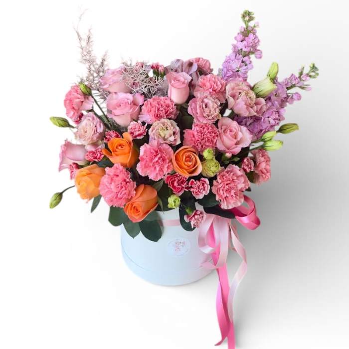 Pink and orange flower arrangement in a white hat box with ribbon