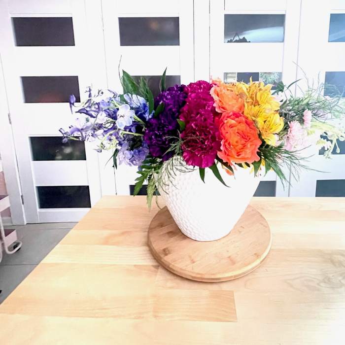 Rainbow floral arrangement in a white vase on a wooden tray