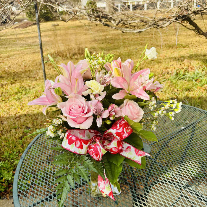 Pink lilies and roses in a glass vase with a floral ribbon