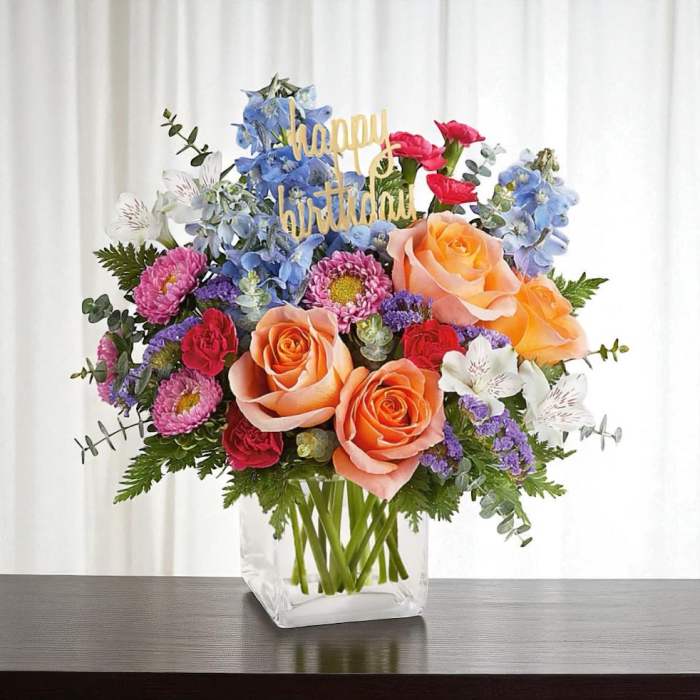 Mixed bouquet of roses, daisies, and blue flowers in a clear vase